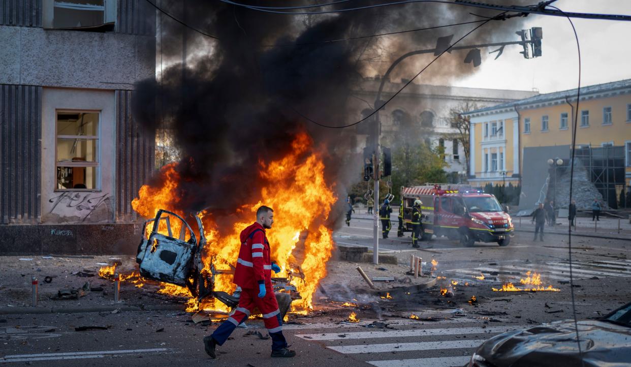 A medical worker runs past a burning car after a Russian attack in Kyiv, Ukraine, Monday, Oct. 10, 2022. 