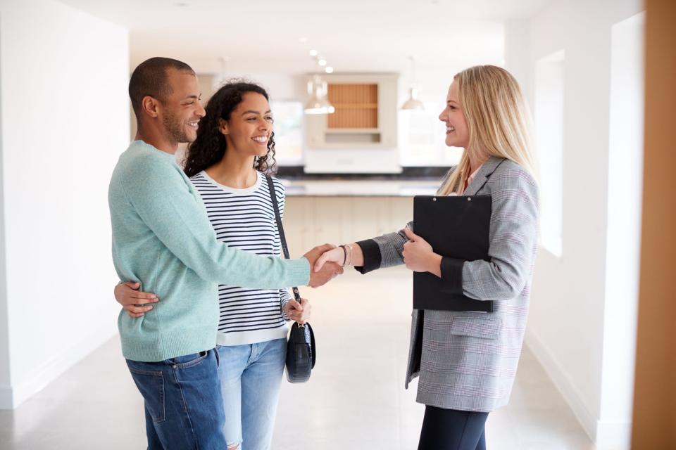 A Realtor shakes hands with a couple interested in buying a house.