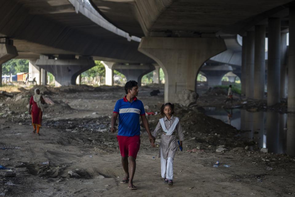 Shiv Kumar, left, accompanies his daughter Garima, 10, to her school as they walk on the flood plain of Yamuna River, in New Delhi, India, Friday, Sept. 29, 2023. Their family was among those displaced by the recent floods in the Indian capital's Yamuna River. (AP Photo/Altaf Qadri)