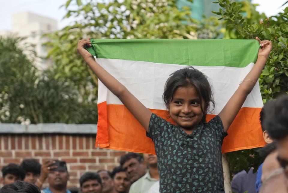 A girl stands with the Indian national flag as she watches a live telecast of the landing og Chandrayaan-3, or “moon craft” in Sanskrit, in Mumbai, India, Wednesday, Aug. 23, 2023. India has landed a spacecraft near the moon’s south pole, an unchartered territory that scientists believe could hold vital reserves of frozen water and precious elements, as the country cements its growing prowess in space and technology. (AP Photo/Rajanish Kakade)