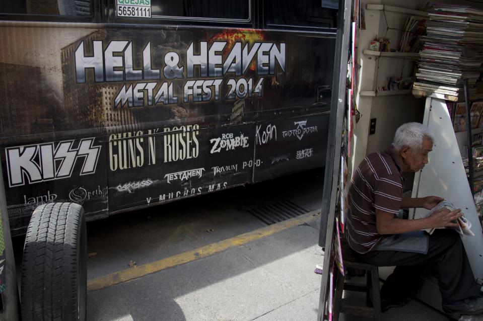 A man reads a newspaper next to publicity of "Hell and Heaven Metal Fest" concert, posted on bus in Mexico City, Friday March 7, 2014. The Mexico state government canceled the concert saying the March 15-16 "Hell and Heaven Metal Fest" planned for a fairground just east of Mexico City did not have adequate safety plans, posing a risk to concert-goers. (AP Photo/Eduardo Verdugo)
