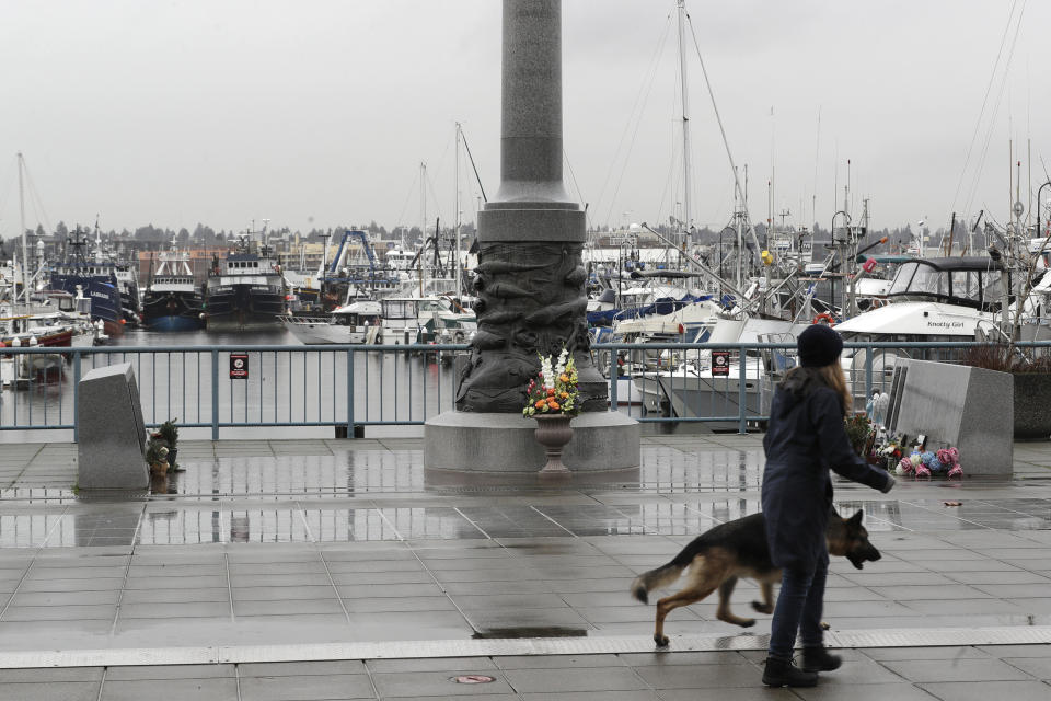 A pedestrian and a dog walk past the Seattle Fishermen's Memorial, Thursday, Jan. 2, 2020, in Seattle. Items left at the memorial Thursday included a ball cap with the name of the crab fishing boat Scandies Rose, a 130-foot crab fishing boat from Dutch Harbor, Alaska, that sank on New Year's Eve. (AP Photo/Ted S. Warren)