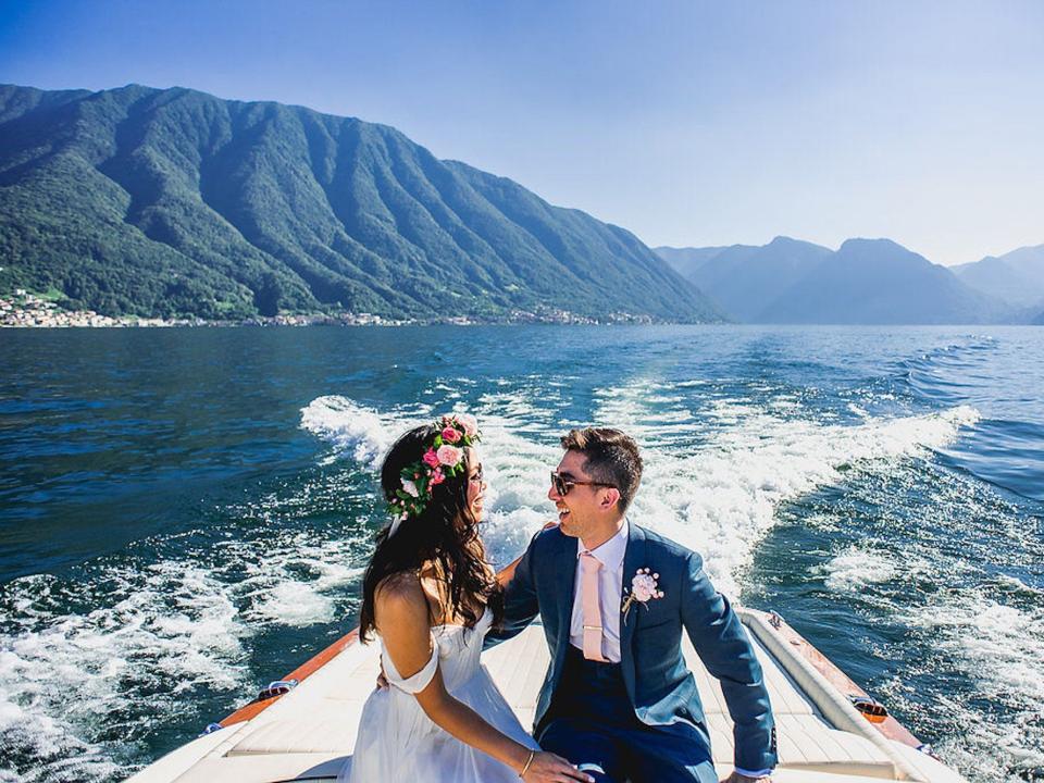 A bride and groom laugh on a boat on Lake Como.