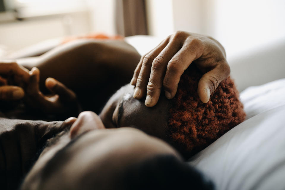 One person comforting another lying in bed, with a gentle hand on their head