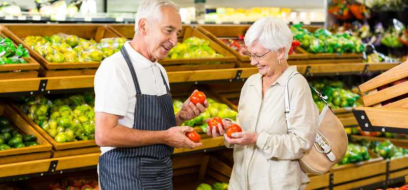 Elderly couple checking out produce in a grocery store.
