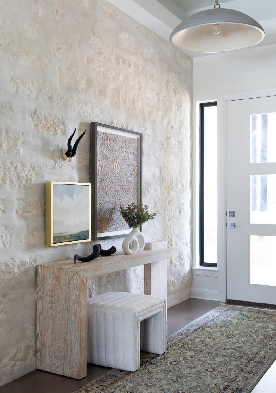 entryway with stone wall, wooden console table with hung art
