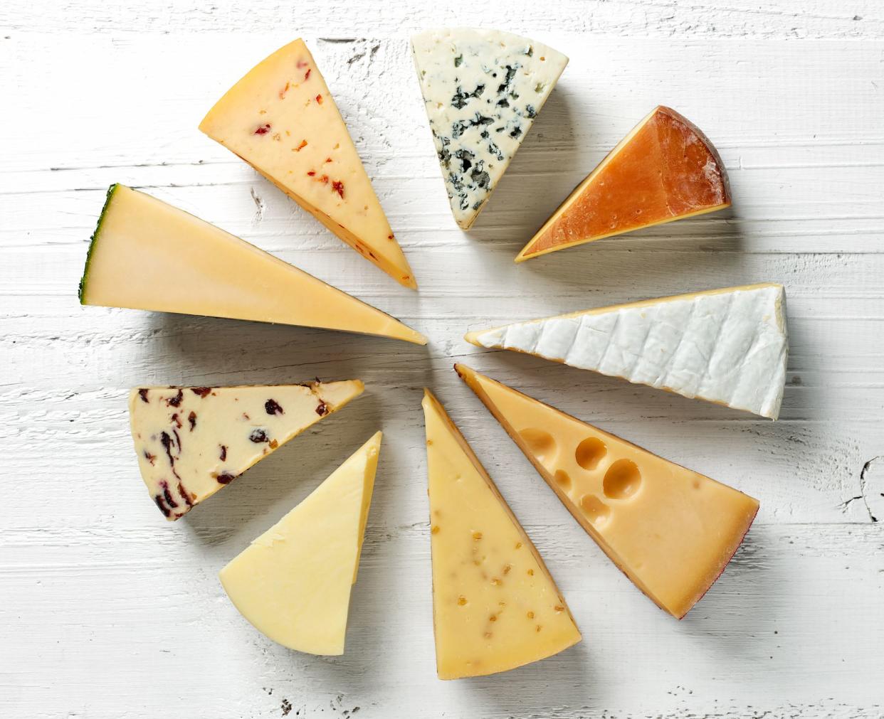 Top view of various types of cheese in a circle on a white wooden table