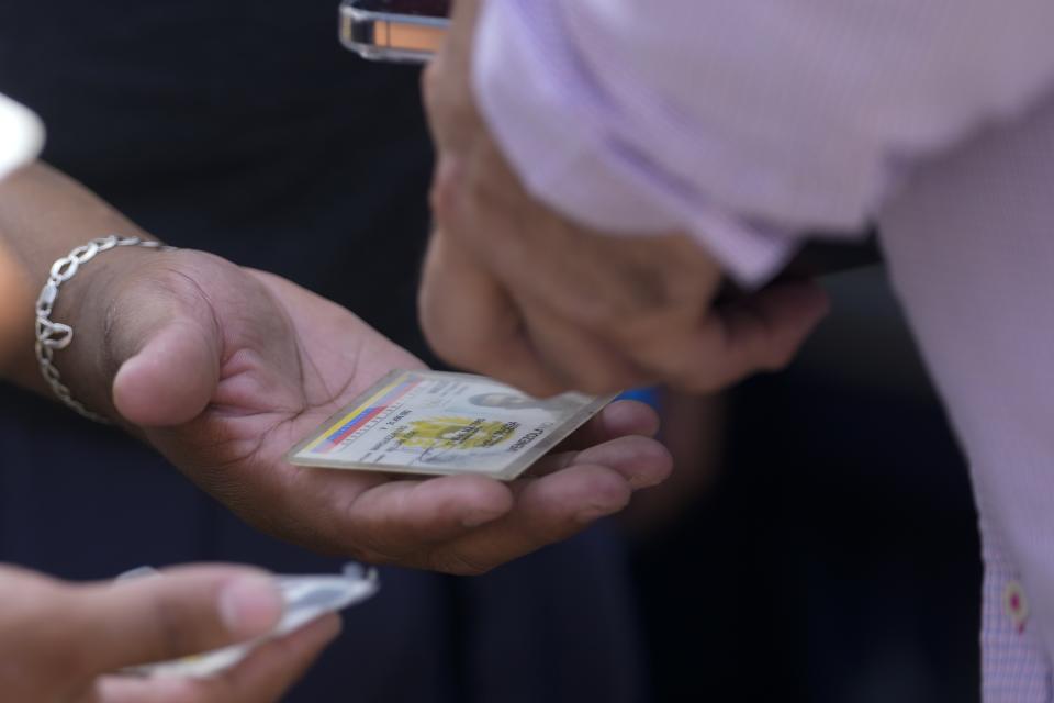 A Venezuelan migrant show his identification card to a Venezuelan official before boarding a bus to the Tocumen International Airport to return to Venezuela, in Panama City, Wednesday, Oct. 26, 2022. (AP Photo/Arnulfo Franco)