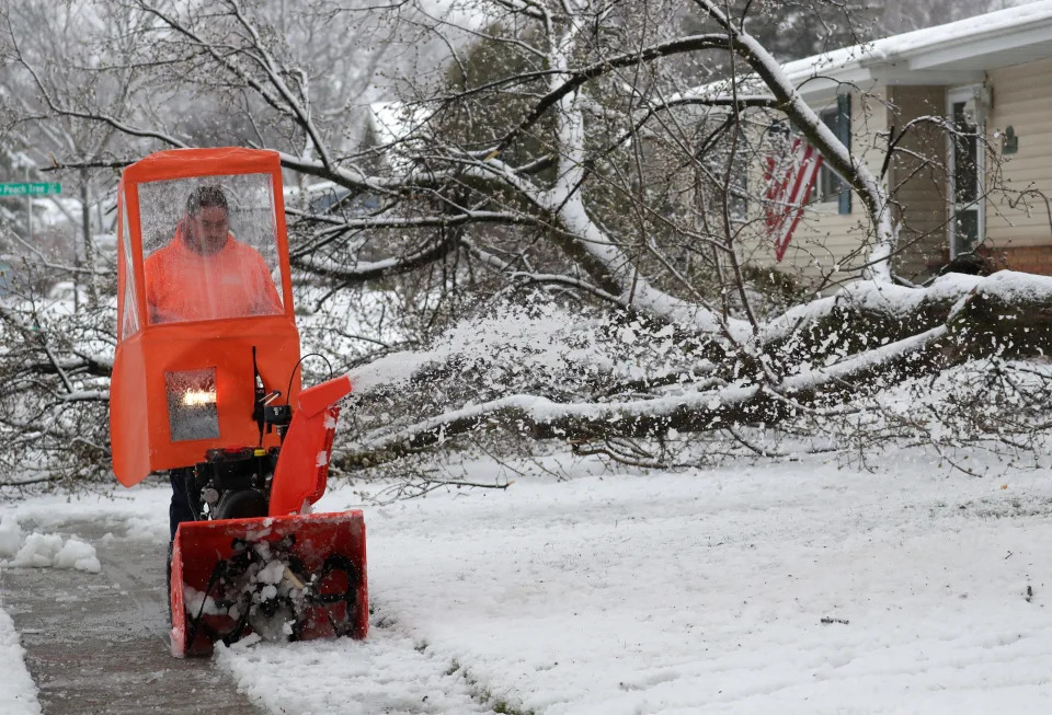 Mike Kuen clears heavy snow from his parents' home after a large limb broke off a tree in their front yard on April 3, 2024, in Appleton, Wisconsin.