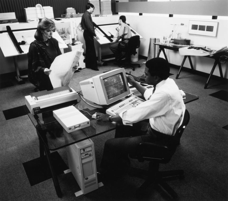 People working in an office, including one person in front of an early PC