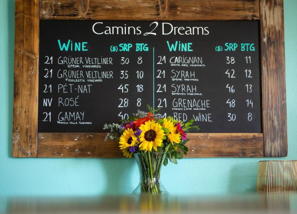 The menu on a chalkboard at Camins 2 Dreams in Lompoc, with a vase of sunflowers in front of it.