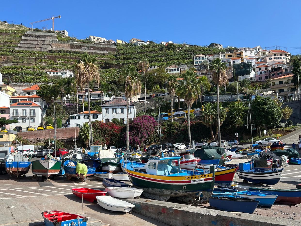 Small boats sitting on a dock. Houses on a mountain are behind the boat.