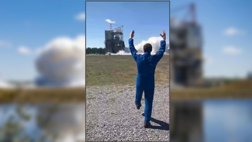 two pictures on top of each other. the top picture shows reid wiseman in a flight suit, from the back, raishing his hands as an engine fires on a test stand far in front of him. the back picture shows a blurry view of steam emitting from a tower during the test