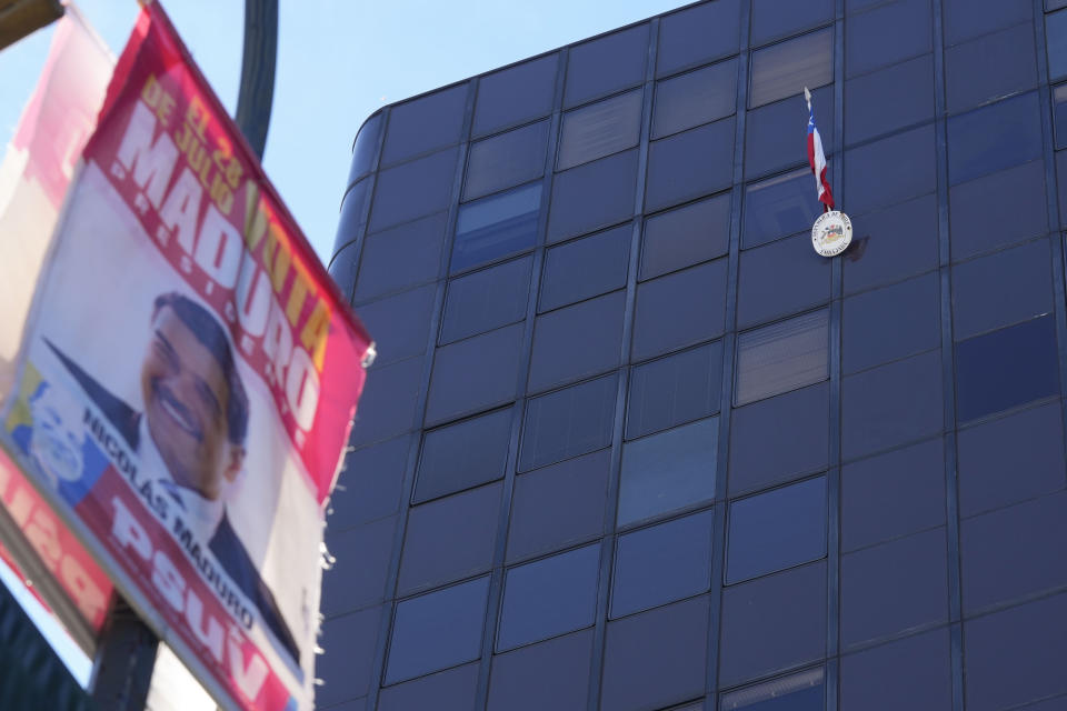 Una bandera chilena cuelga afuera de la embajada de Chile, arriba a la derecha, encima de un cartel de campaña electoral del presidente venezolano Nicolás Maduro en un poste de luz en Caracas, Venezuela, el martes 30 de julio de 2024. (AP Foto/Fernando Vergara)