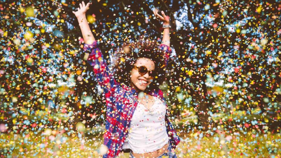 Young mixed race woman jumping for joy in a park as confetti falls around her