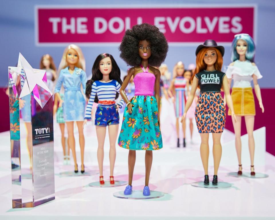 Several Barbie dolls on stands lined up together.