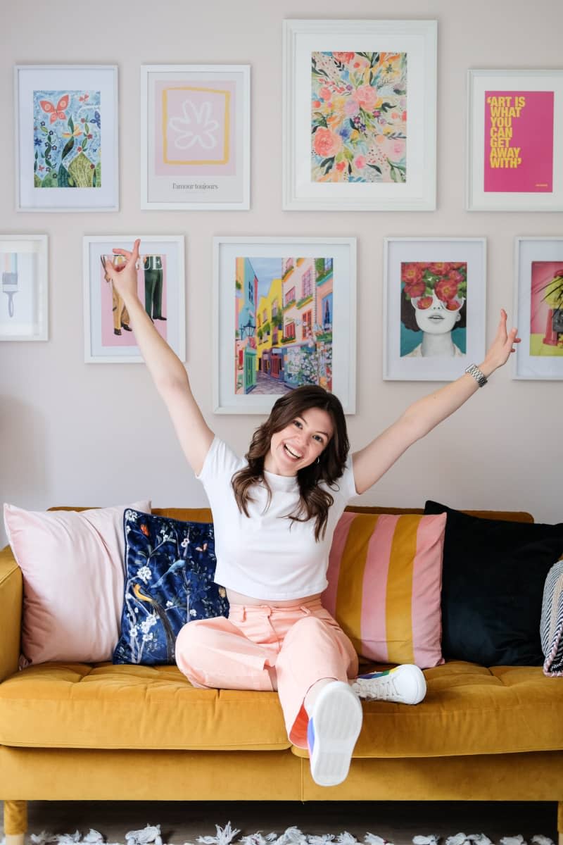 gallery wall above yellow couch with pink and yellow striped and blue throw pillow