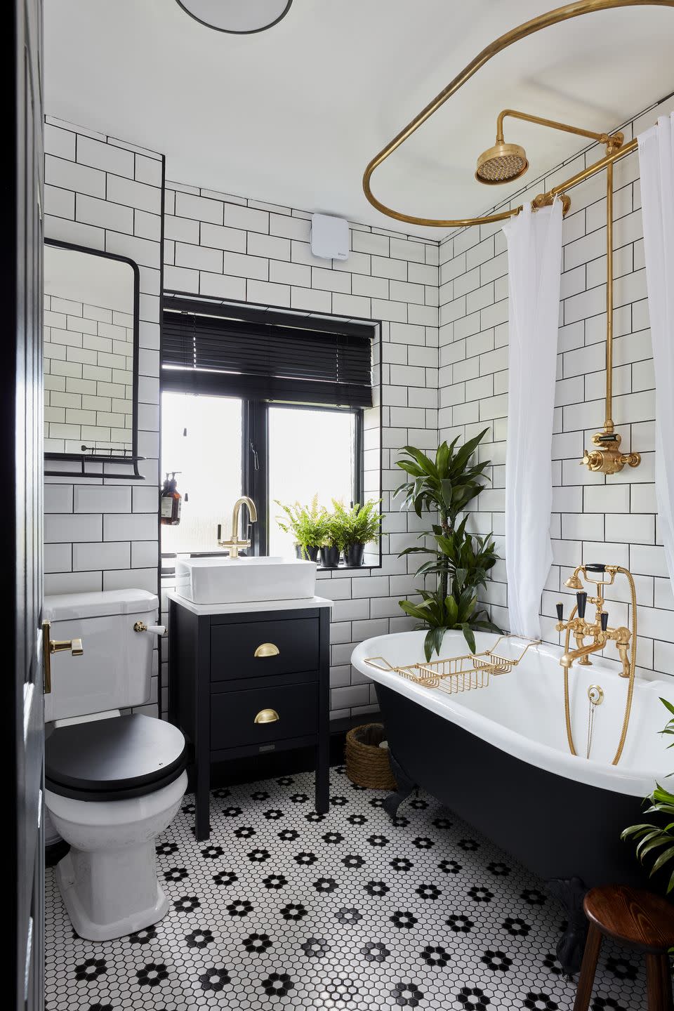 monochrome bathroom with patterned daisy print tiles, brass fittings and a black freestanding bathtub