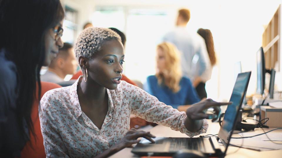 Closeup side view of two mid 20's  black women doing their design project on a computer.