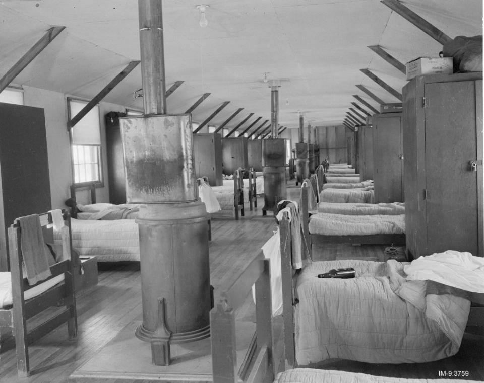 The interior of an army barracks with rows of beds, lockers and wood-fire stoves in the center aisle. National Security Research Center