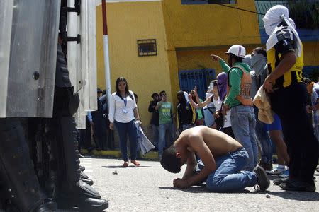 A boy with blood on his chest kneels in front of police after 14-year-old student Kluiver Roa died during a protest in San Cristobal February 24, 2015. REUTERS/Carlos Eduardo Ramirez