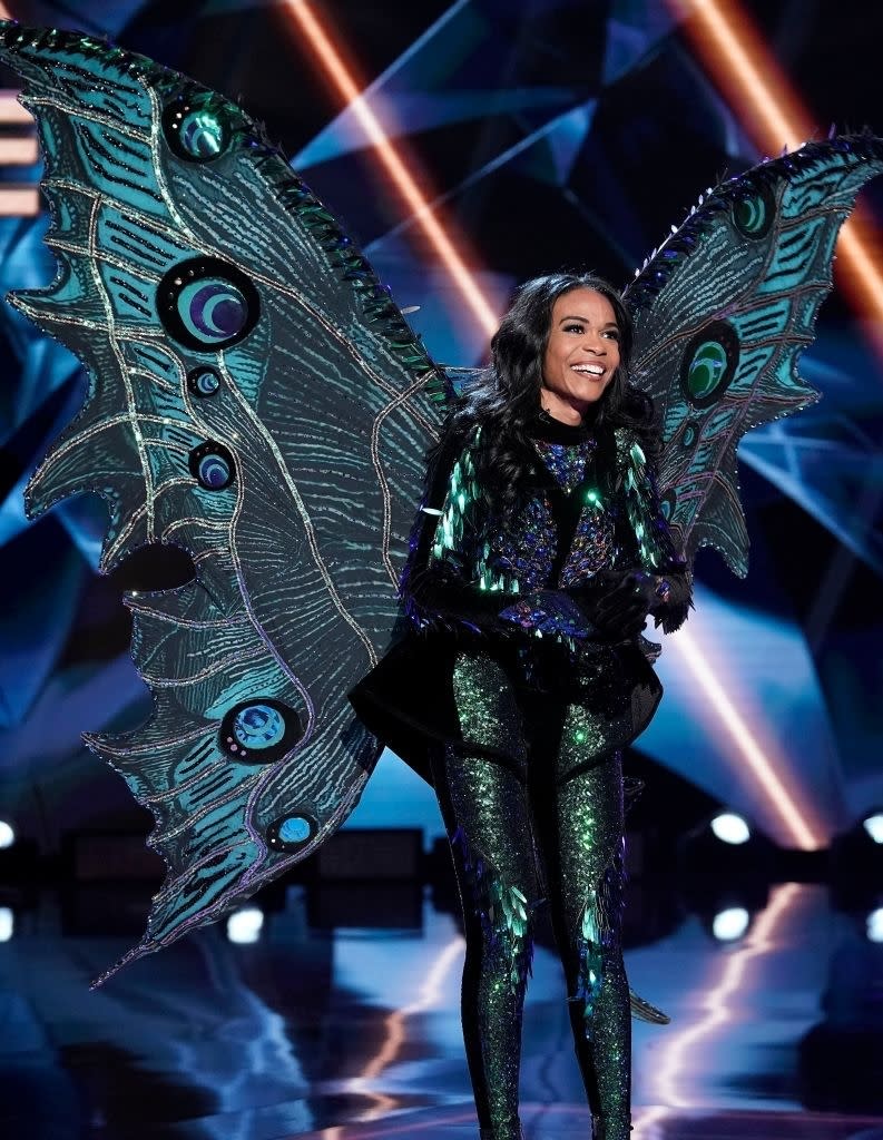 Michelle Williams dressed in a sparkling bodysuit with large, intricate butterfly wings, performing on stage