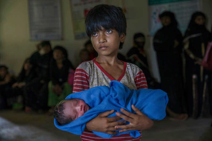 FILE – In this Sept. 13, 2017, file photo, Rohingya Muslim girl Afeefa Bebi, who crossed over from Myanmar into Bangladesh holds her few-hours-old brother as doctors check her mother Yasmeen Ara at a community hospital in Kutupalong refugee camp, Bangladesh. A new report by the United Nations children’s agency says the lives and futures of more than 19 million Bangladeshi children are at risk from colossal impacts of devastating floods, cyclones and other environmental disasters linked to climate change. The UNICEF report released Friday, April 5, 2019 said the tally includes Rohingya refugee children from Myanmar who are living in squalid camps in southern Bangladesh. (AP Photo/Dar Yasin, File)