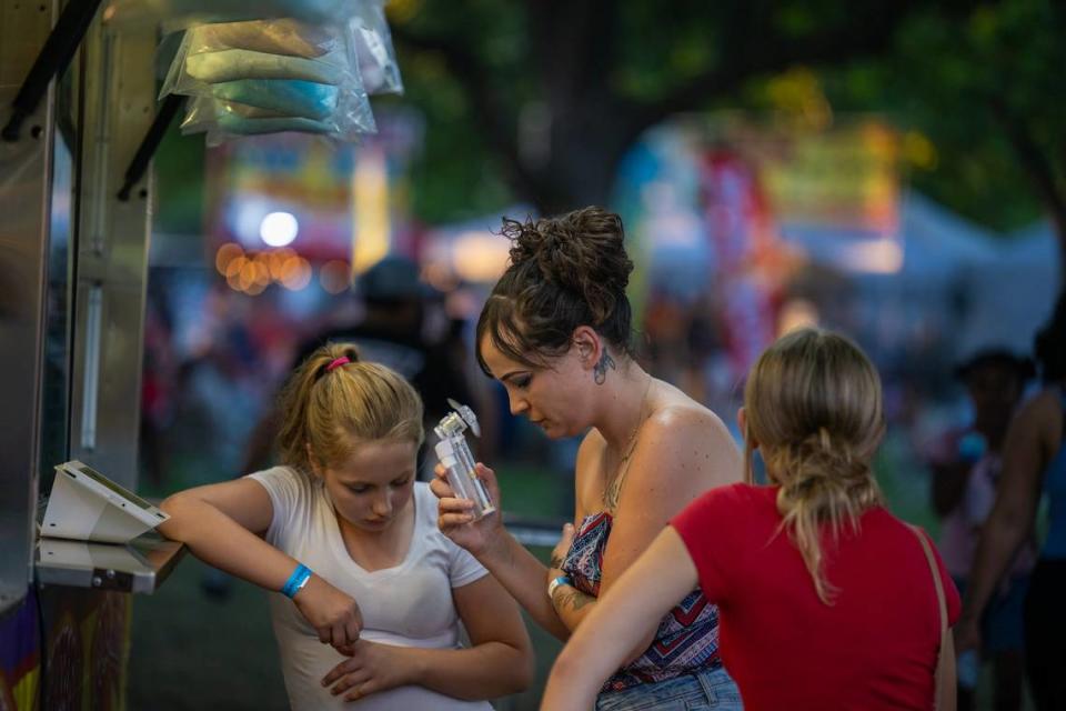 Kayla Abrahams, center, cools herself with an electric fan as she waits with daughters Ciara, left, 10, and Jaycee, 12, for refreshments at a food stand at the Rancho Cordova Fourth of July celebration on Wednesday in Hagan Park.