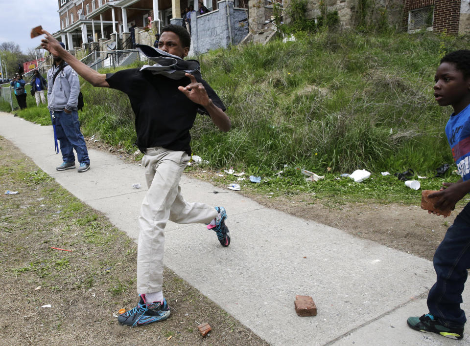 A boy throws a brick at police, Monday, April 27, 2015, during unrest following the funeral of Freddie Gray in Baltimore. Gray died from spinal injuries about a week after he was arrested and transported in a Baltimore Police Department van. (AP Photo/Patrick Semansky)