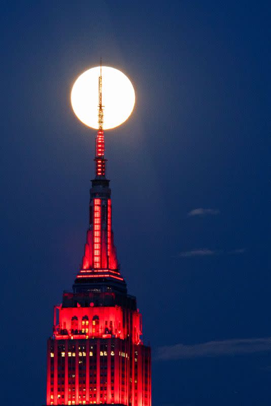 The Supermoon rises behind the Empire State Building while it glows red in solidarity with those infected with coronavirus as the outbreak of the disease (COVID-19) continues in the Manhattan borough of New York City, as it is seen from Hoboken