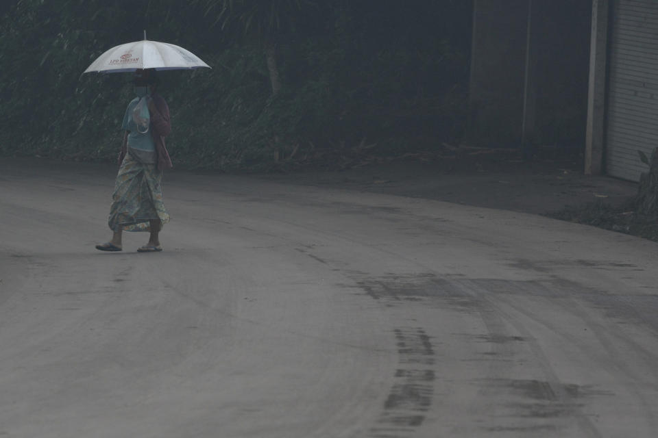 A woman uses an umbrella on Saturday as she walks through ash spewed by the volcano.