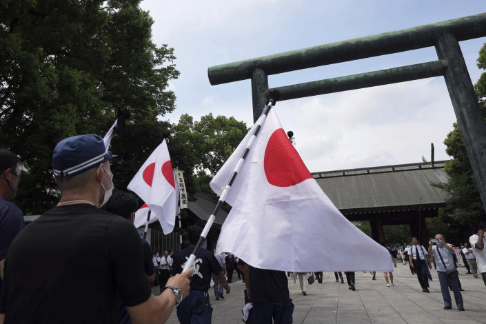 People hold Japanese flags as they walk in Yasukuni Shrine Monday, Aug. 15, 2022, in Tokyo. Japan marked the 77th anniversary of its World War II defeat Monday. (AP Photo/Eugene Hoshiko)