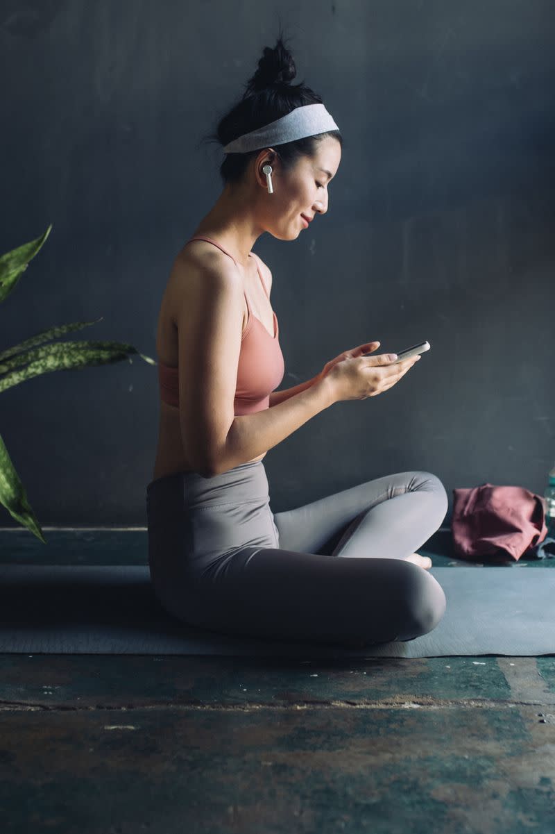 A woman sits on an exercise mat with her mobile phone