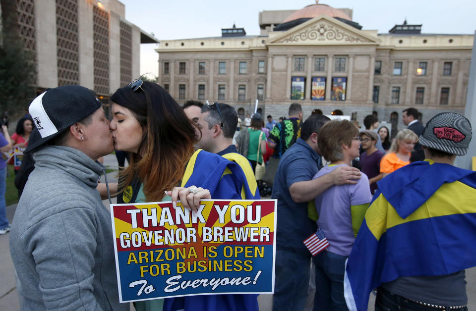 With the Arizona Capitol in the background, gay rights supporters Rachel Butas, right, and Jo Jo Halko kiss after the two learn that Arizona Gov. Jan Brewer announces she has vetoed SB1062, a bill designed to give added protection from lawsuits to people who assert their religious beliefs in refusing service to gays, on Wednesday, Feb. 26, 2014, in Phoenix. (AP Photo/Ross D. Franklin)