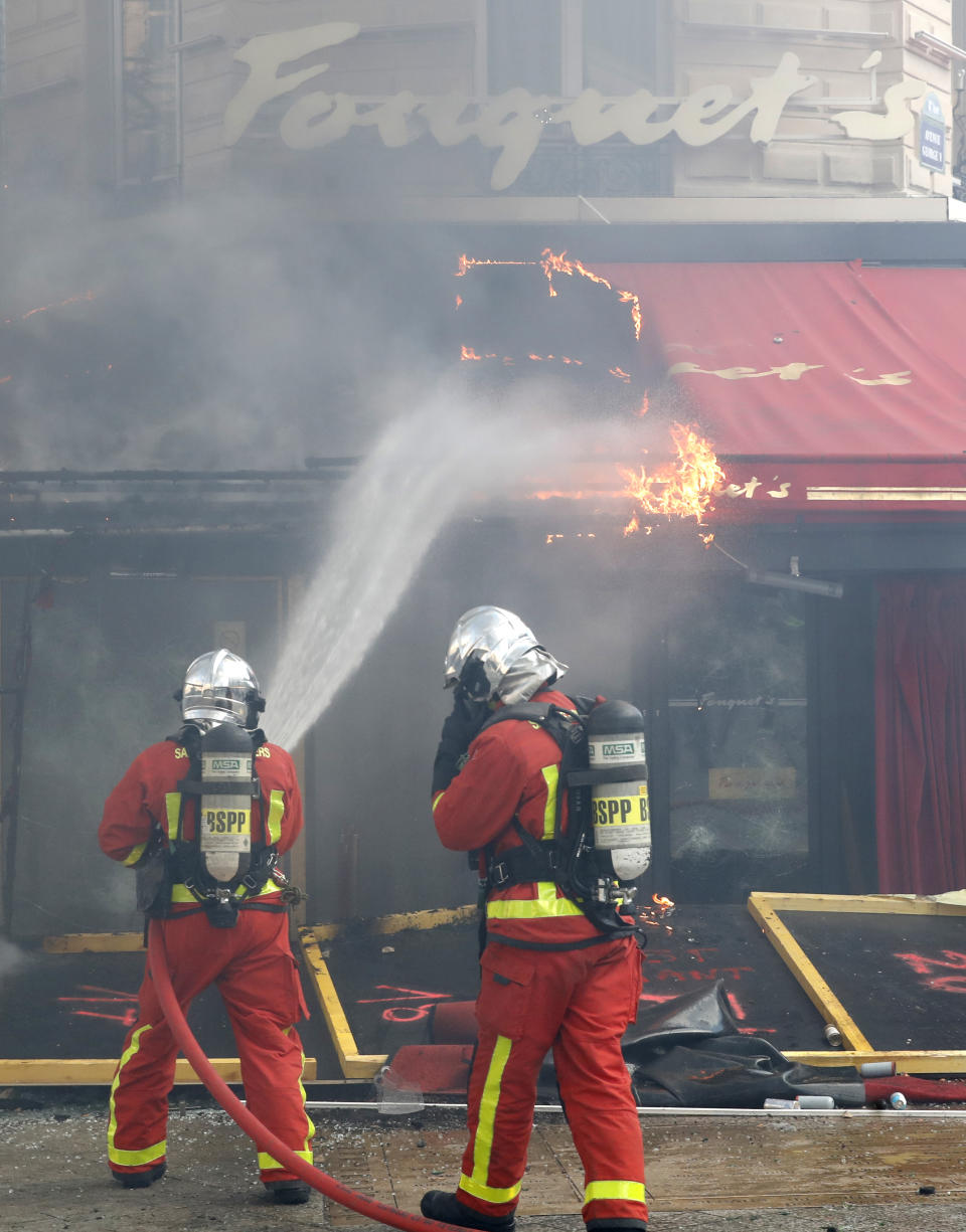 Firefighters try to pull off a fire on the famed restaurant Fouquet's, on the Champs Elysees avenue, during a yellow vests demonstration Saturday, March 16, 2019 in Paris. Paris police say more than 100 people have been arrested amid rioting in the French capital by yellow vest protesters and clashes with police. They set life-threatening fires, smashed up luxury stores and clashed with police firing tear gas and water cannon (AP Photo/Christophe Ena)