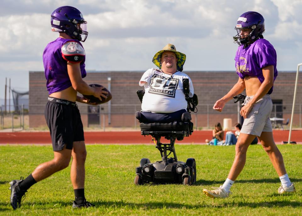 Wickenburg High School junior Clayton Smid (left) hands off the ball to senior Luke Drescher (right) as assistant football coach Carter Crosland observes during practice at the school's football field.