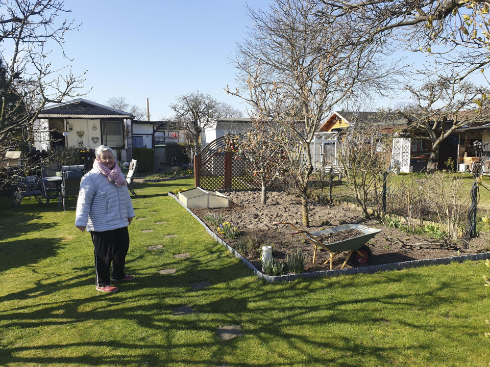 In this Feb. 24, 2020 photo, Heidi Schaletzky stands on the lawn near a cherry tree in her garden in Berlin, Germany. The garden is one of about 67,000 strewn across Berlin. Many were created on the edge of the city during the early 20th century to feed the capital's growing population of workers and give them an opportunity to exercise outside their often cramped apartments. They remain a treasured part of Berlin life, especially for retirees like the Schaletzkys. In order to slow down the spread of the coronavirus, the German government has considerably restricted public life and asked the citizens to stay at home and keep distance from other people. (AP Photo/Frank Jordans)