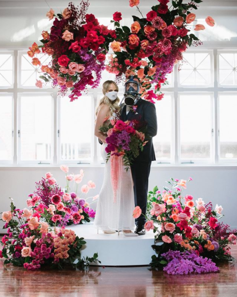 Couple on a floral stage in their bride and groom outfits and face masks