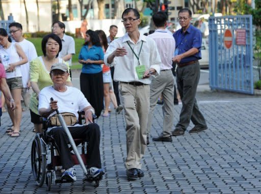 A presiding officer leads a voter in a wheelchair to a polling centre in Singapore. Singapore's ruling People's Action Party (PAP) was returned to power on Sunday with a huge majority but lost a key district to the opposition, costing a senior cabinet minister his job