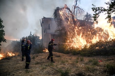 Firefighters try to extinguish a fire burning near a house as a wildfire burns at the village of Kontodespoti