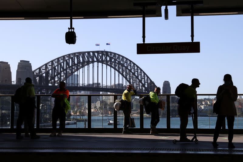 Commuters wait on a train platform in front of the Sydney Harbour Bridge at Circular Quay in Sydney