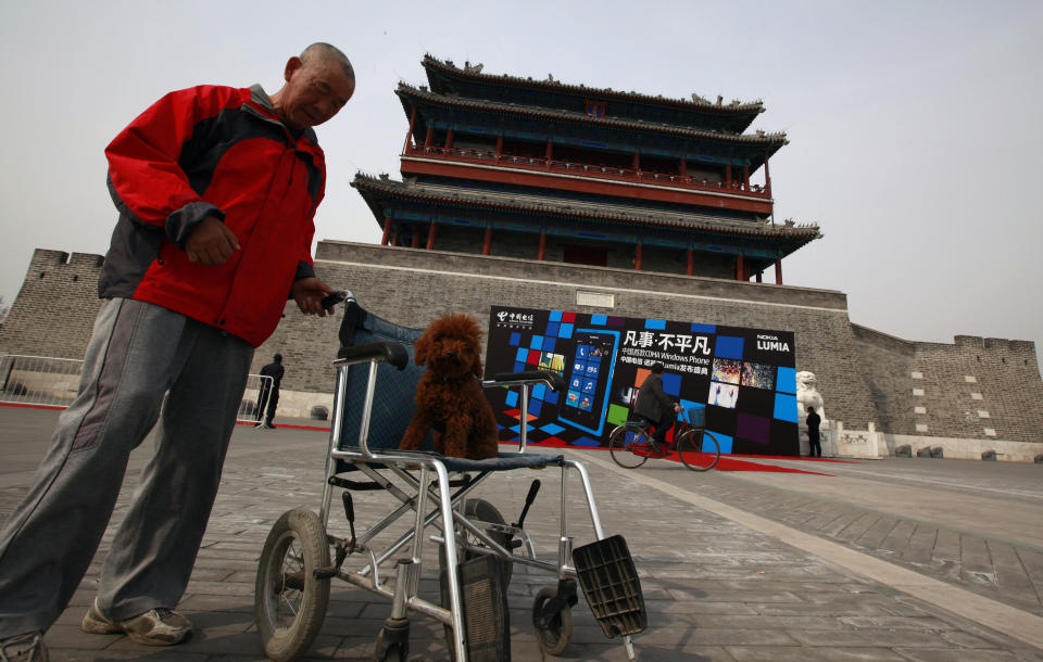 A Chinese man pushes his dog on a wheelchair past the venue of the Nokia product launch in Beijing, China, Wednesday, March 28, 2012. Struggling cellphone maker Nokia launched its first smartphone design for China on Wednesday, looking to the world's biggest mobile market to help drive a turnaround.(AP Photo/Ng Han Guan)