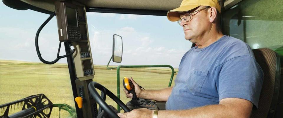 Farmer driving combine and harvesting crop.