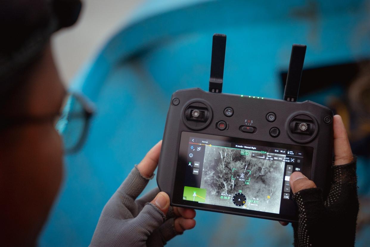 An over-the-shoulder shot of a researcher from the mosquito project gazing at the remote control screen of a thermal imaging drone camera he is flying over the jungle, close to the Danau Girang Research Centre, Kinabatangan, Sabah