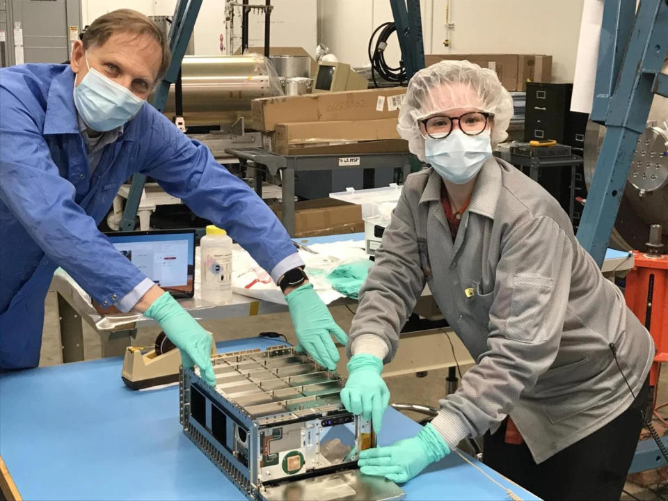 Two scientists in a lab wearing lab gear and holding the satellite.