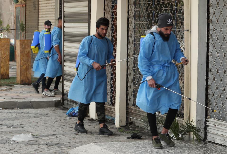 Iraqi volunteers spray disinfectant as a precaution against the coronavirus during a curfew, in a market in Baghdad, Iraq, Sunday, March 22, 2020. (AP Photo/Hadi Mizban)
