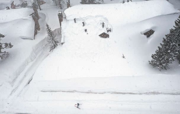 PHOTO: A skier passes by as workers remove snow from the roof of a condominium complex in the Sierra Nevada mountains after another storm system brought heavy snowfall, March 29, 2023, in Mammoth Lakes, Calif. (Mario Tama/Getty Images)