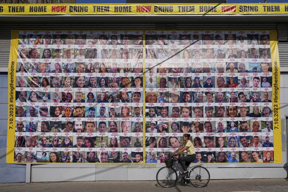 A woman cycles next to a billboard calling for the return of about 240 hostages who were abducted during the Oct. 7, Hamas attack on Israel. in Tel Aviv, Israel on Friday, Nov. 24, 2023. Friday marks the start of a four-day cease-fire in the Israel-Hamas war, during which the Gaza militants pledged to release 50 hostages in exchange for 150 Palestinians imprisoned by Israel. (AP Photo/Ohad Zwigenberg)