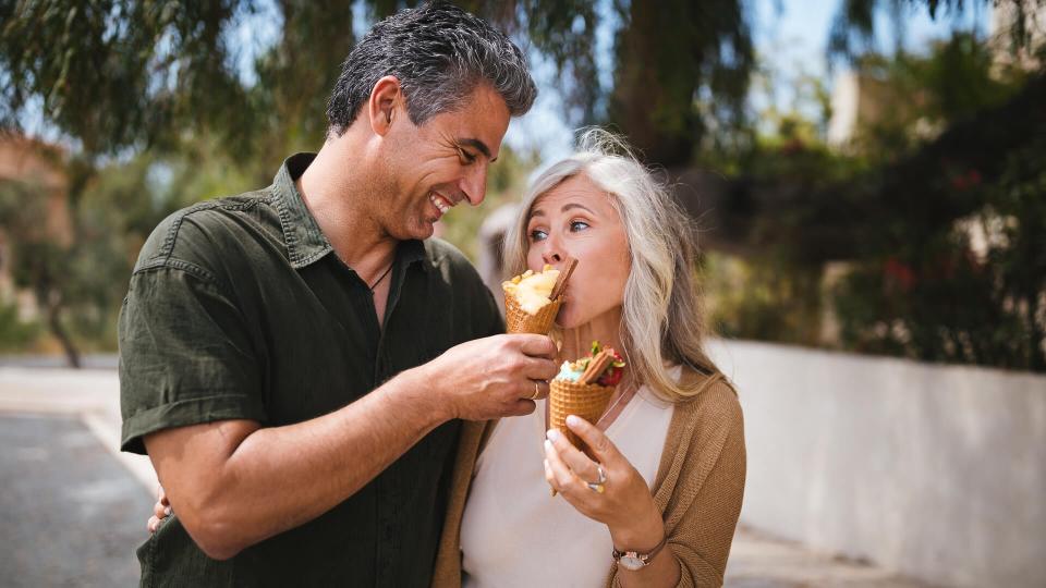 Happy mature husband and wife having fun eating ice cream together on sunny day in spring.