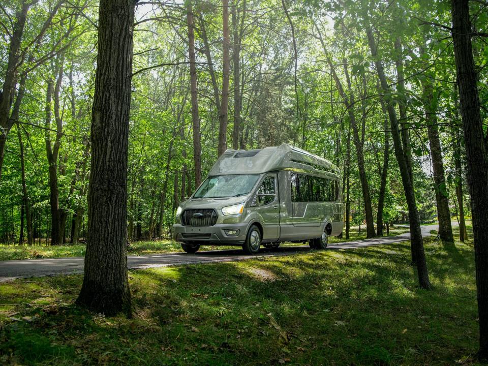 The concept Thor Vision Vehicle camper van driving on a road among tall green trees.